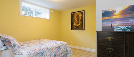A bedroom with a bed, a dresser, a window, and two wall art pieces.