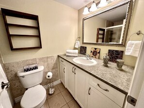 Une salle de bain avec des toilettes, un lavabo et un miroir. On y trouve un porte-serviettes et une étagère au-dessus du lavabo.