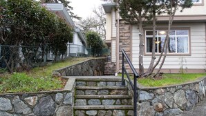 Un escalier en pierre mène à une maison dont la façade est bordée d’un mur de soutènement en pierre.