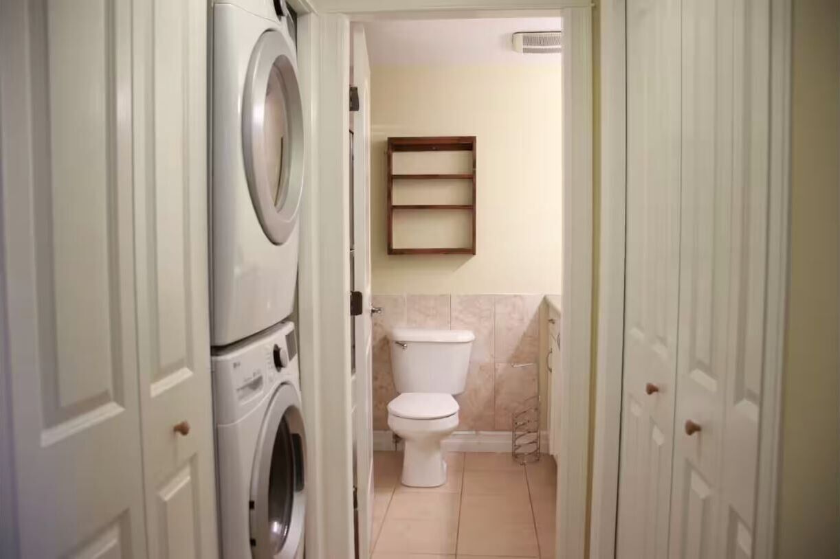 A laundry room with a washing machine and dryer, a toilet, and a shelf above the toilet.