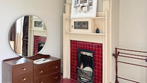 Una habitación con un aparador de madera, un espejo, una chimenea con baldosas rojas y una obra de arte enmarcada sobre la chimenea.