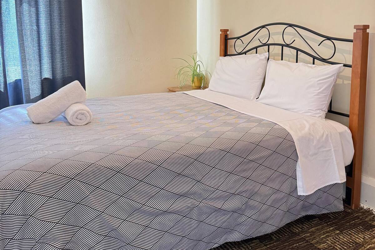 Una cama bien hecha con una colcha estampada, una toalla blanca enrollada y dos almohadas blancas.