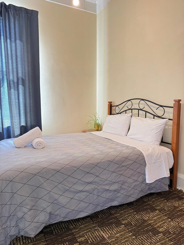 Un letto rifatto con cura, una coperta a motivi, un asciugamano bianco arrotolato e due cuscini bianchi.