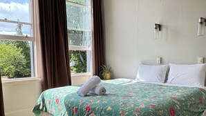 Una cama bien hecha con colcha estampada, una ventana con cortinas y una lámpara de pared.