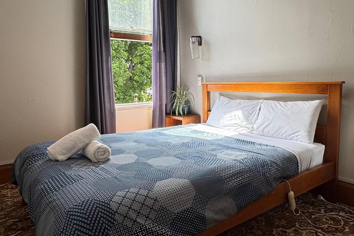 Una cama bien hecha con una colcha estampada y una toalla enrollada al lado.