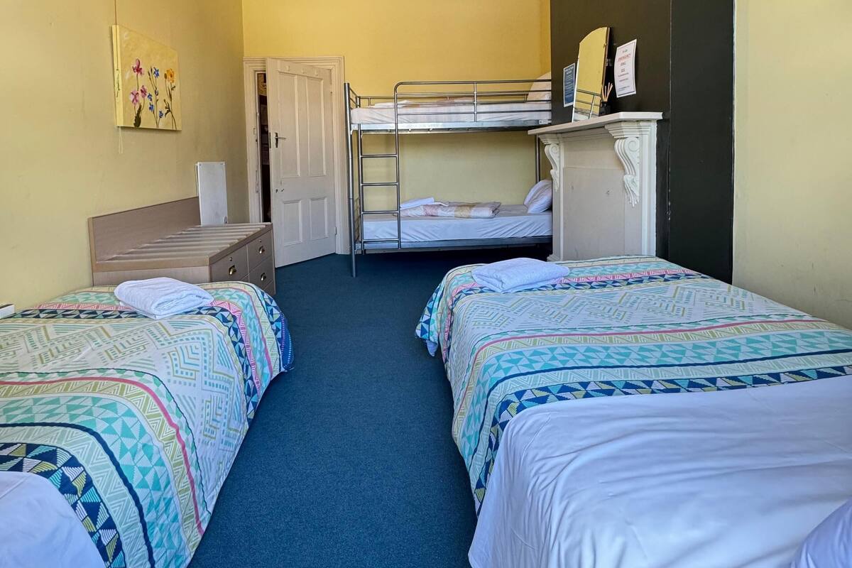Habitación de hotel con dos camas, un escritorio, una silla, un armario y un cuadro en la pared.