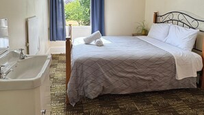 Un dormitorio con cama, una ventana con cortinas, un lavabo y una lámpara fijada a la pared.