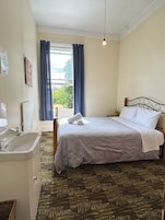 Um quarto com cama, janela com cortinas, pia e luminária na parede.