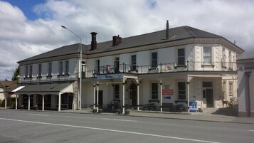 Um edifício de dois andares com varanda no andar térreo, placa indicando bar e restaurante, e uma rua na frente.