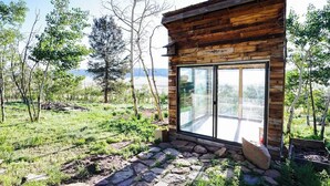 A rustic cabin with a large glass door and stone pathway leading to it.