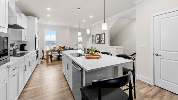 Cocina moderna con armarios blancos, una isla central, iluminación colgante y vistas al exterior.