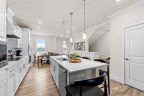 Een moderne keuken met witte kasten, een centraal eiland, hangende verlichting en uitzicht op de omgeving.