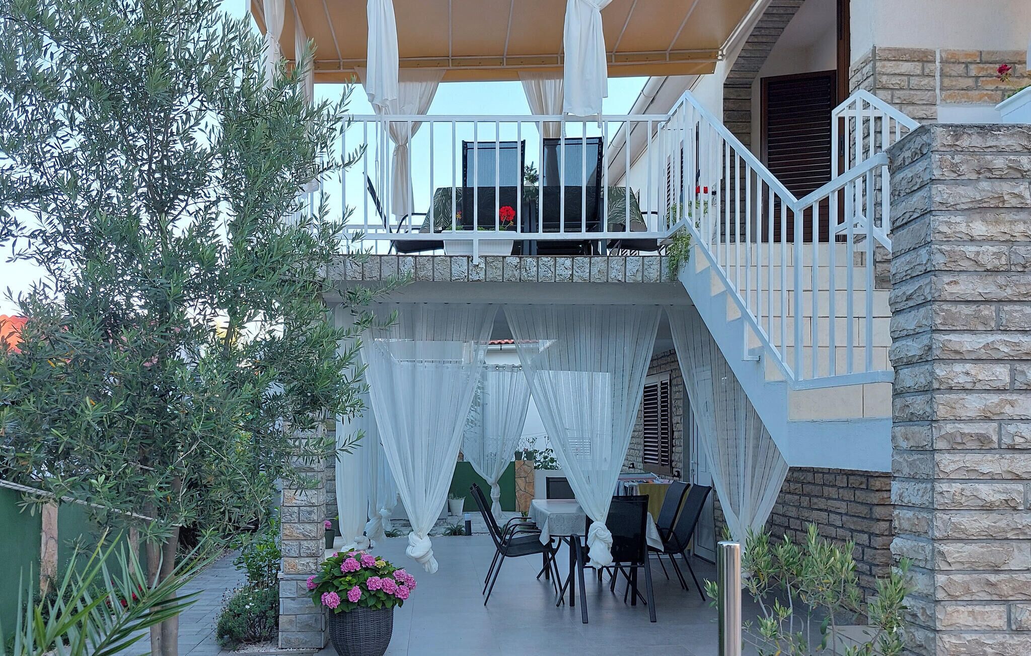 Eine überdachte Terrasse mit Esstisch und Stühlen, ein kleiner Gartenbereich mit Pflanzen und eine Steinmauer.