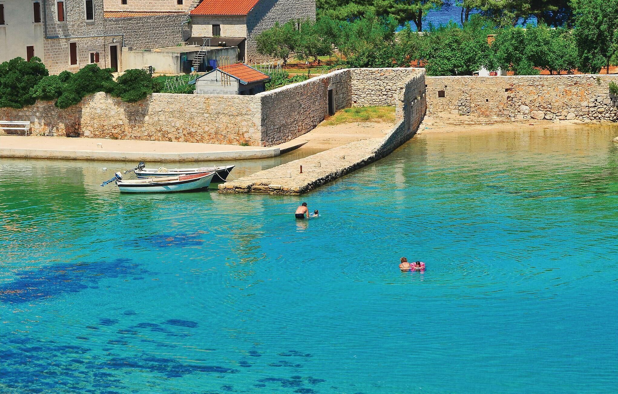 A coastal scene with a stone wall, a small boat docked near the shore, and a clear blue body of water.