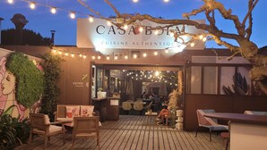 En uteservering med ljusslingor, trägolv och en skylt för restaurangen ”CASA DE BON”.