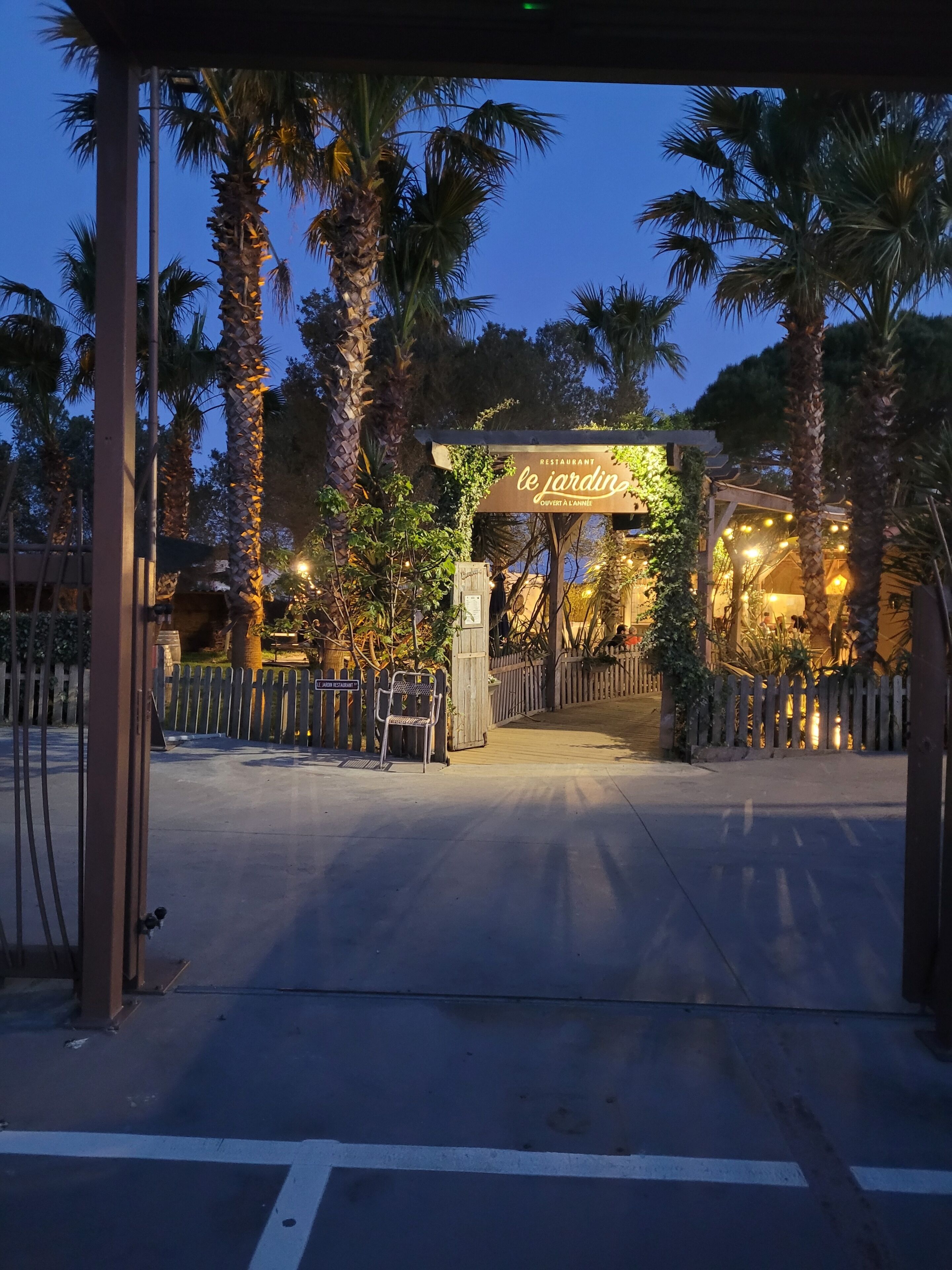 L’entrée d’un restaurant, avec une enseigne, des palmiers et une clôture en bois.