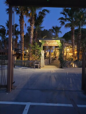 A restaurant entrance with a sign, palm trees, and a wooden fence. - Air-conditioned mobile home at a 4-star campground (Torreilles)
