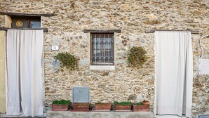 Ein Gebäude aus Stein mit einem Fenster, Vorhängen und Topfpflanzen.