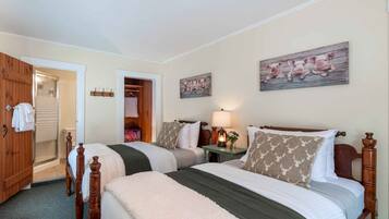 Quarto com duas camas, guarda-roupa de madeira, banheiro com chuveiro e corredor com cabideiro.