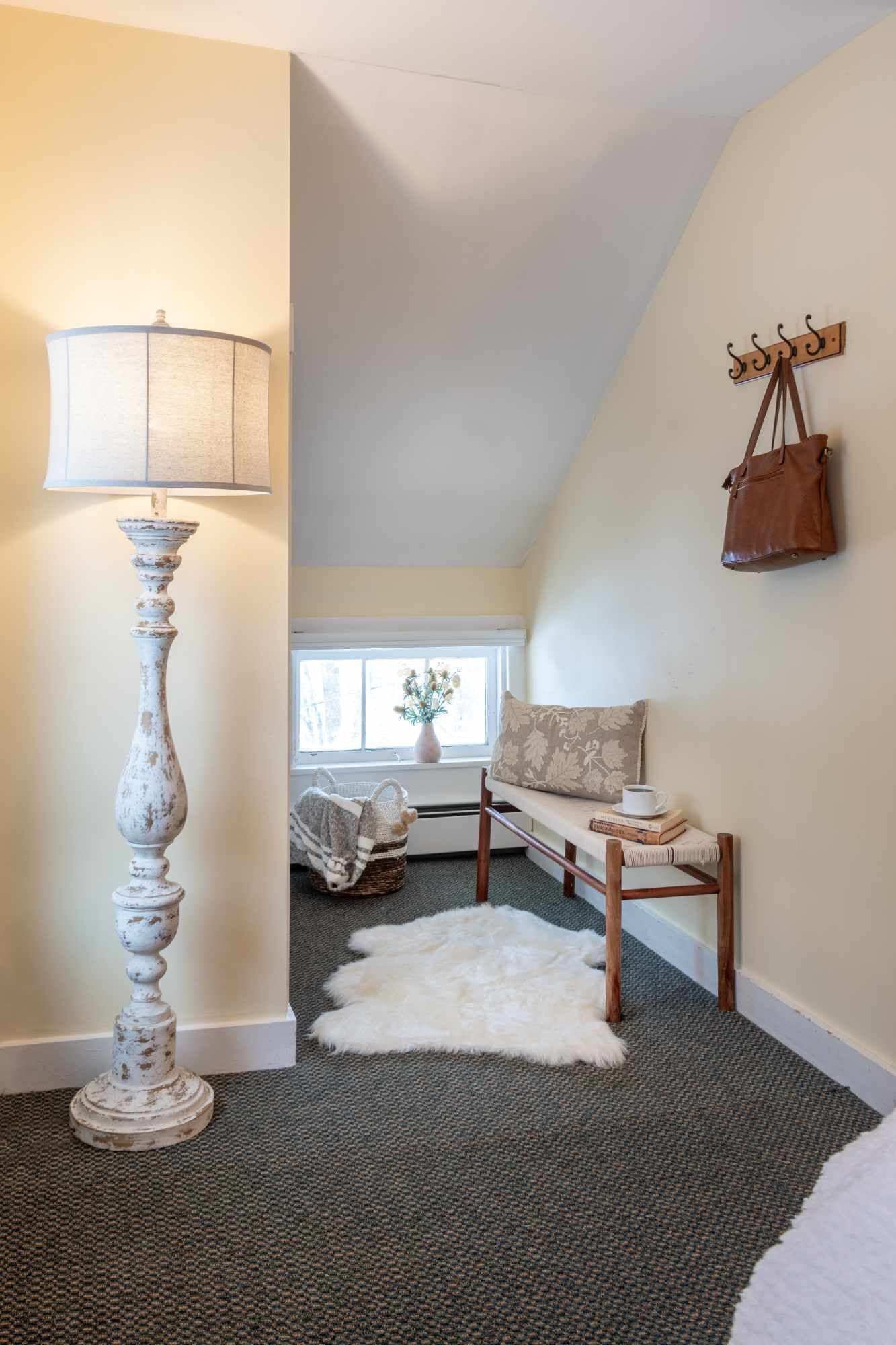 A cozy room with a lamp, a bench, a handbag, and a fur rug.