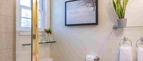 A modern bathroom with a glass shower enclosure, a toilet, a radiator, a sink, and a potted plant.