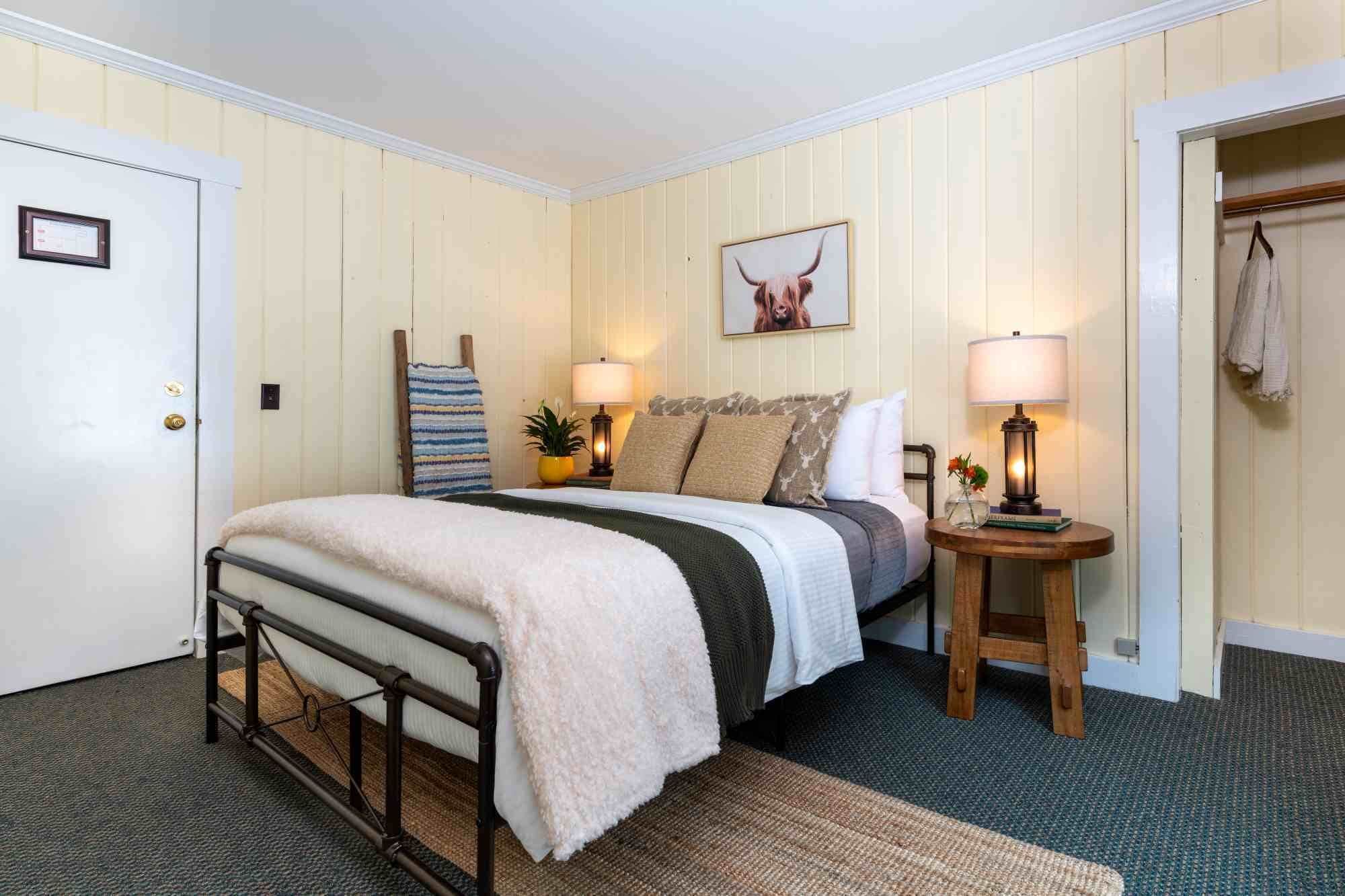 Un dormitorio con una cama, lámparas de noche, una mesita con lámpara, un cuadro en la pared y una puerta.