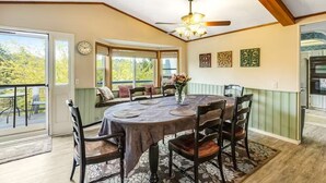 Zona pranzo con tavolo rotondo, sedie, ventilatore a soffitto e vista panoramica attraverso ampie finestre.