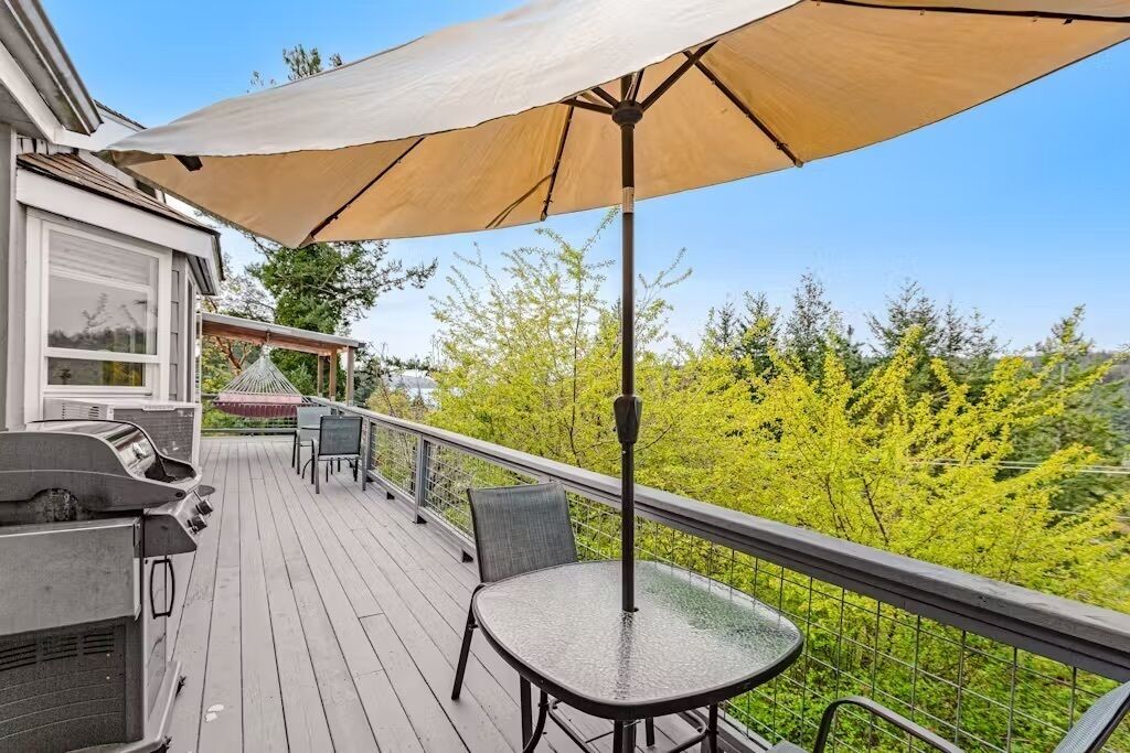 A wooden deck with a grill, a table, and an umbrella.