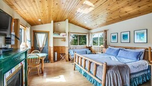 A wooden cabin interior with a bed, a TV, and a dining area. - Deer Harbor Cottages, Entire Property. Sleeps up to 16. 3 Hot Tubs. 4 Bedrooms. (Eastsound)