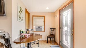 A dining area with a round table, chairs, a window with blinds, and a door with a metal gate. - Sunset Suite in Deer Harbor (Eastsound)