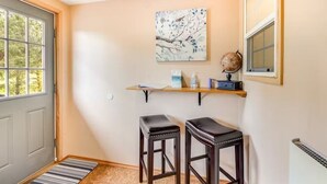 A small, well-lit room with a wooden door, a window, a shelf with a globe and decorative items, and two stools. - Sunset Suite in Deer Harbor (Eastsound)