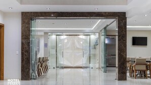 Eine Hotellobby mit Glastür, einer Rezeption und einer Sitzecke mit Stühlen.