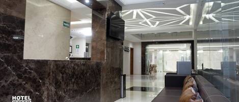 Rebedor modern d'hotel amb taulell de recepció, zona de seients i una partició de vidre.