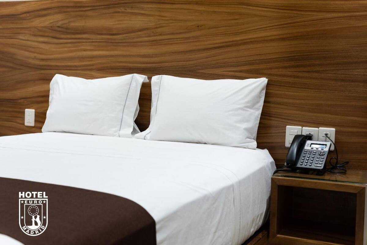 Ein Hotelzimmer mit Holz-Kopfteil, weißer Bettwäsche und Telefon am Nachttisch.