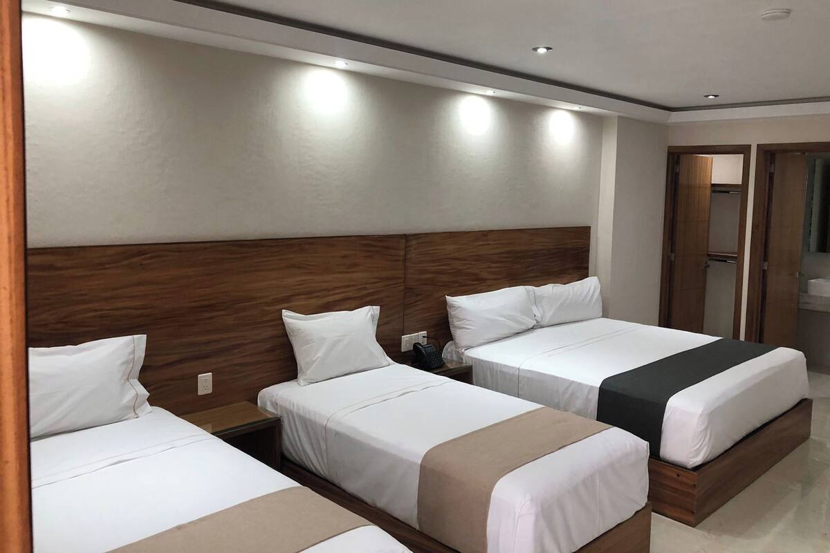 Ein Hotelzimmer mit drei Einzelbetten, einem Holz-Kopfteil und einem Spiegel an der Wand.
