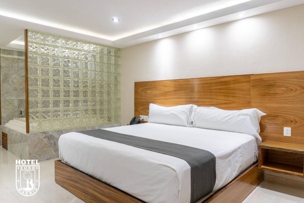 Ein modernes Hotelzimmer mit einem großen Bett, einem Holzkopfteil und einer Trennwand aus Glas.