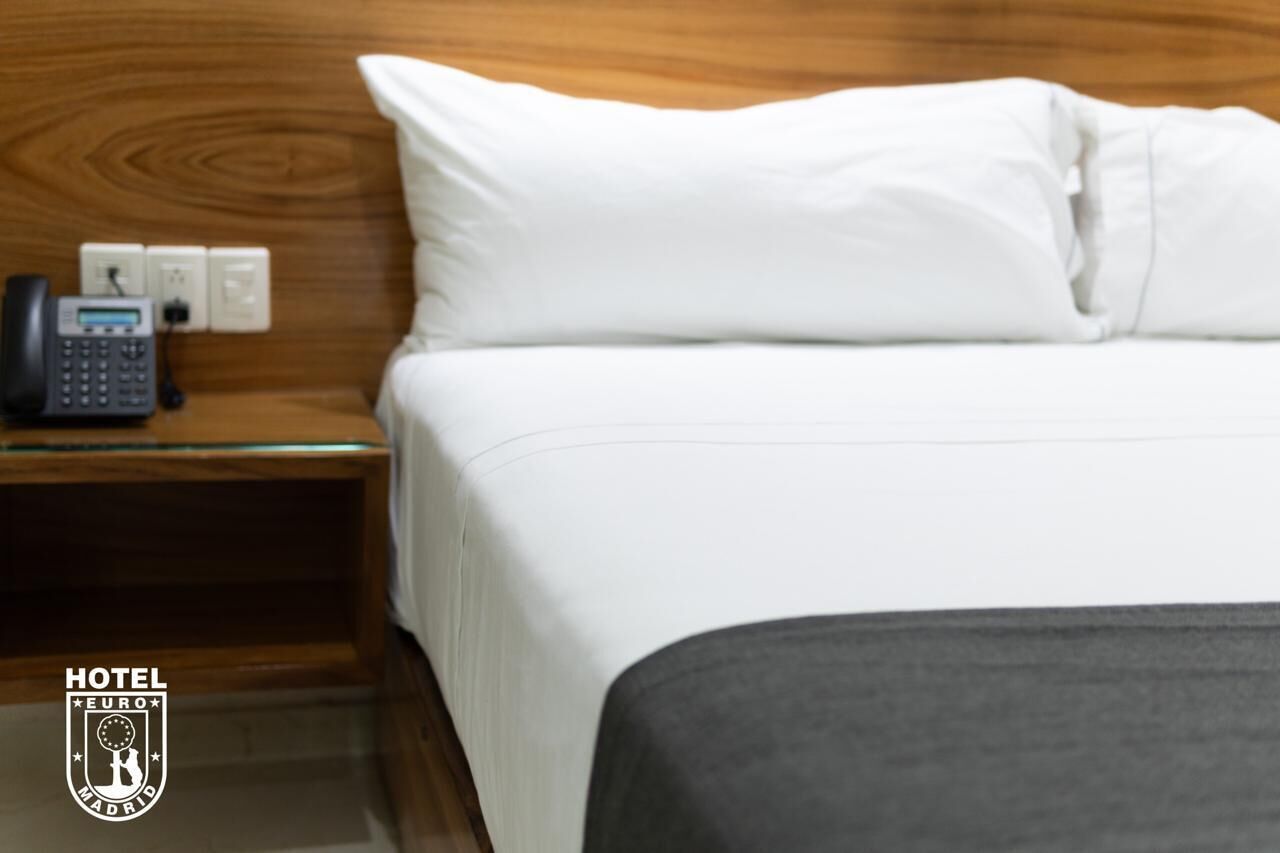 A hotel room with a neatly made bed, a bedside telephone, and a wooden headboard.