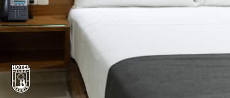 A hotel room with a neatly made bed, a bedside telephone, and a wooden headboard.