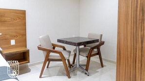 Ein Eckzimmer mit einem Holzkopfteil, einer kleinen Holzablage, einem runden Tisch mit zwei Stühlen und einer weißen Wand.