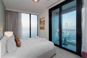 Een moderne hotelkamer met een groot bed, een balkon met uitzicht op een reuzenrad en water, en een schilderij aan de muur.