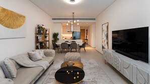 Un salon moderne comprenant un canapé, un pouf, une table basse, un téléviseur et un coin repas avec des chaises et une table.