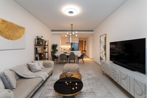 Un salon moderne comprenant un canapé, un pouf, une table basse, un téléviseur et un coin repas avec des chaises et une table.