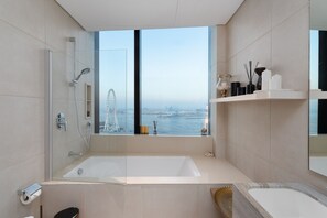 Een moderne badkamer met een ruime badkuip, douche en uitzicht op een stadsgezicht en water.