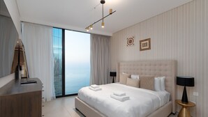 Une chambre d’hôtel moderne, dotée d’un grand lit, d’un bureau, d’une chaise, d’une lampe et offrant une vue sur la ville par la fenêtre.