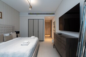 A modern hotel room with a large bed, a dresser, a flat-screen TV, and a walk-in closet.