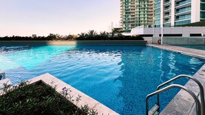 Une piscine à l’eau d’un bleu cristallin, entourée d’un bâtiment moderne doté de balcons.