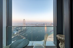 Een hoog gelegen kamer met een groot raam dat uitkijkt over een stadslandschap aan het water, inclusief een brug en een strand.