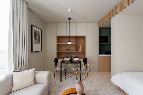 Une chambre d’hôtel moderne comprenant un canapé, une table à manger avec des chaises, un petit coin cuisine et un lit.
