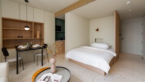 Een moderne hotelkamer met een groot bed, een zithoek met een tafel en stoelen, een kitchenette en een klein werkplek.