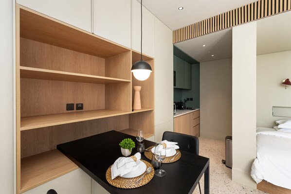 A modern hotel room with a dining area, a bed, and a kitchenette.
